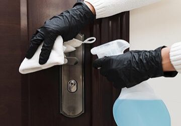 Gloved hands cleaning door handle with spray.